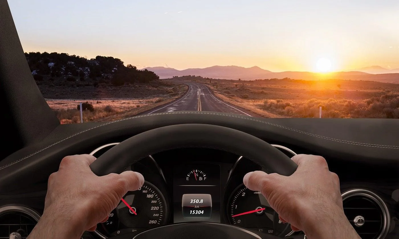 Ruke na volanu dok automobil vozi ka zalasku sunca