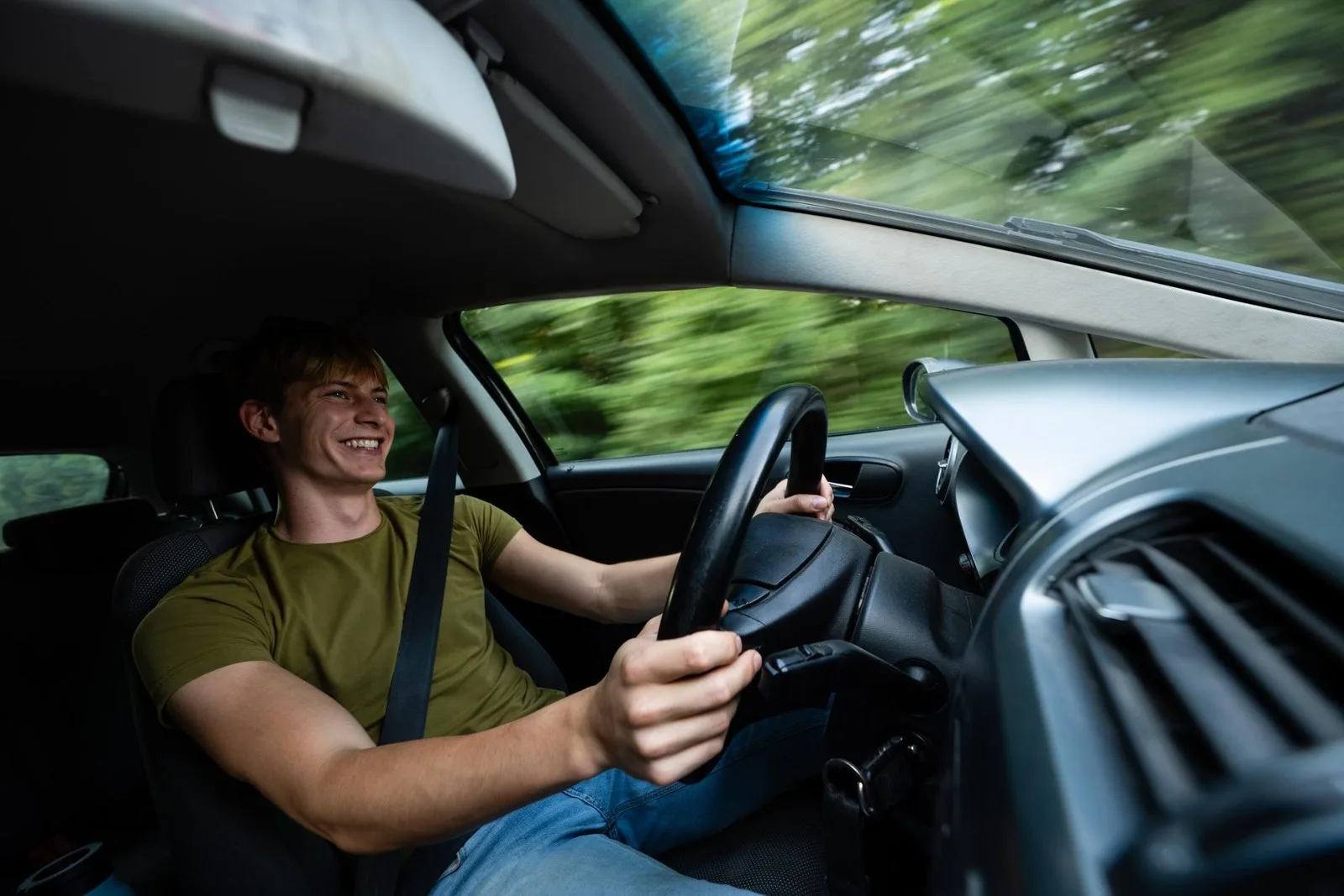 A smiling young man at the wheel of a car