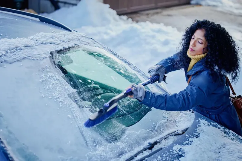 A woman brushing snow off a car windscreen